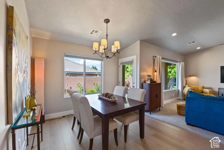 Open-concept living area featuring light wood-finish flooring, a contemporary chandelier, recessed lighting, and large windows