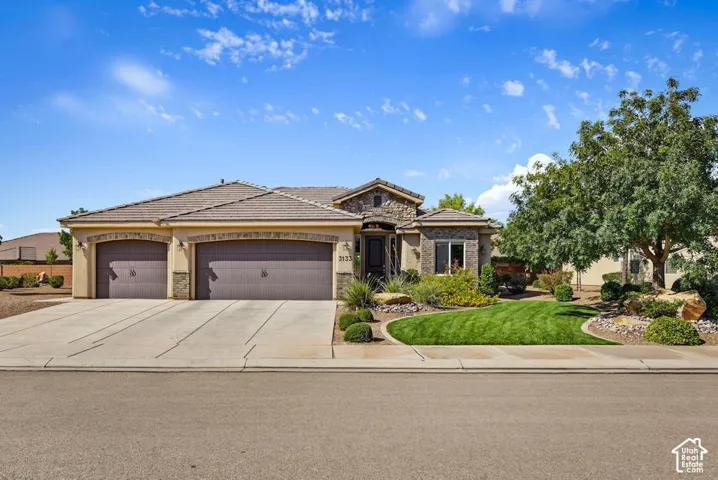 Stucco exterior with stone accents, mature landscaping, a two-car garage, and a concrete driveway