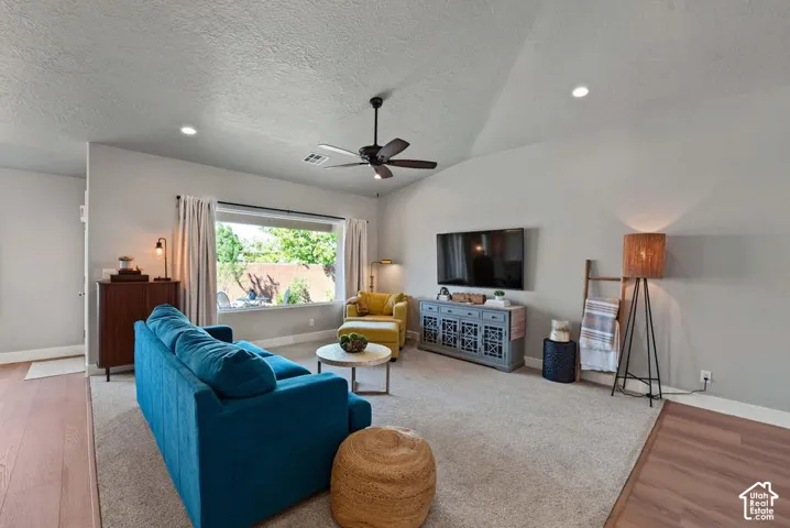Vaulted ceiling with recessed lighting and ceiling fan, large picture window, and wood-finish flooring
