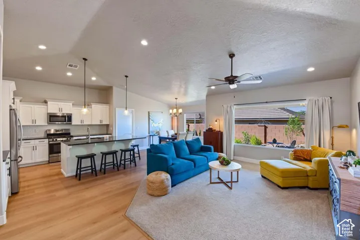 Open-concept living area featuring a kitchen with white cabinetry, stainless steel appliances, a center island with pendant lighting, and wood-finish flooring