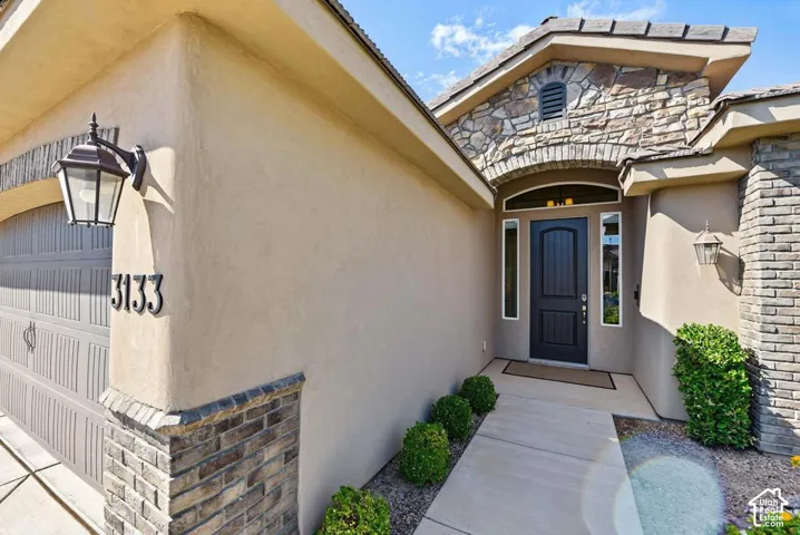 Stucco exterior with stone accents, arched entryway, dark-paneled front door with sidelights, and a garage with overhead lighting