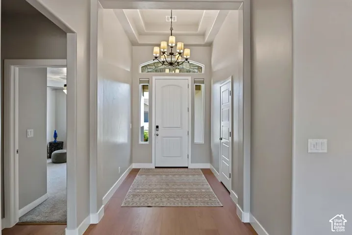 Entryway featuring wood-finish flooring, a coffered ceiling, a multi-tier chandelier, a white paneled door, and sidelight windows