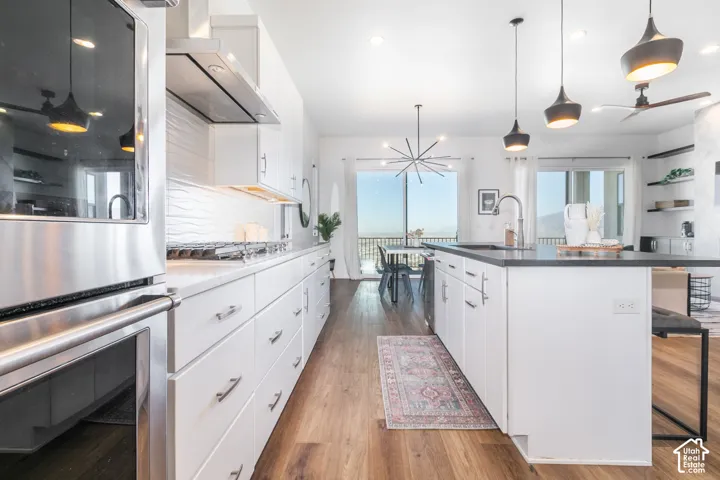Stainless steel appliances, wood-finish flooring, white cabinetry, dark countertops, and a white textured backsplash