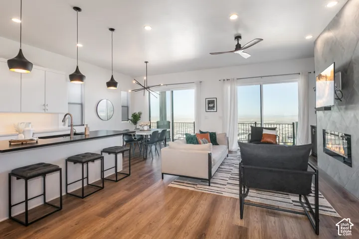 Open-concept living space featuring a chef's kitchen with white cabinetry, stainless steel appliances, and large island with quartz countertops. Living room with electric fireplace, and dining area with sliding glass door out to the deck.