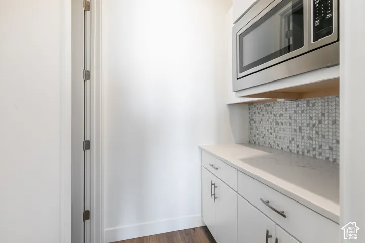 Butler kitchen with built in stainless steel microwave, white cabinetry with silver hardware, white countertop, and mosaic tile backsplash