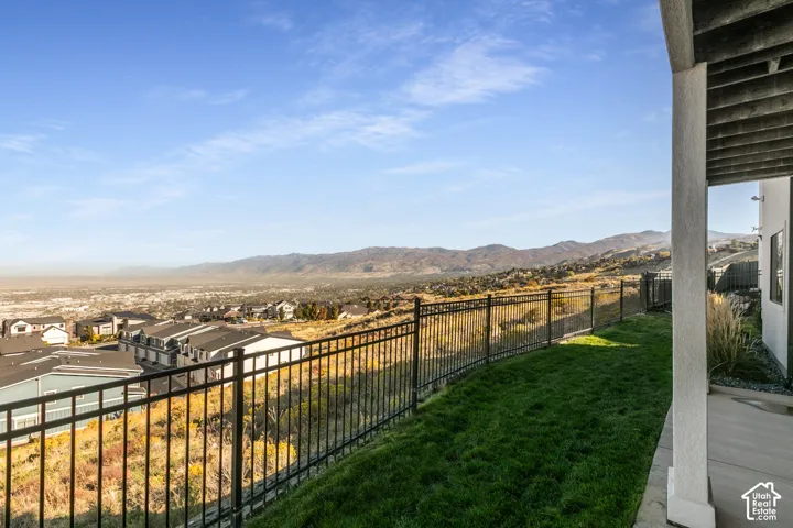 Expansive backyard space featuring a sloped lawn, black metal fencing, a concrete patio, and distant mountain scenery
