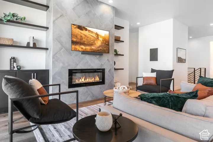 Modern living space featuring a linear gas fireplace with stone surround, wall-mounted flat-screen television, floating shelving with integrated storage, engineered wood-finish flooring, and a curved lounge chair with metal frame accents