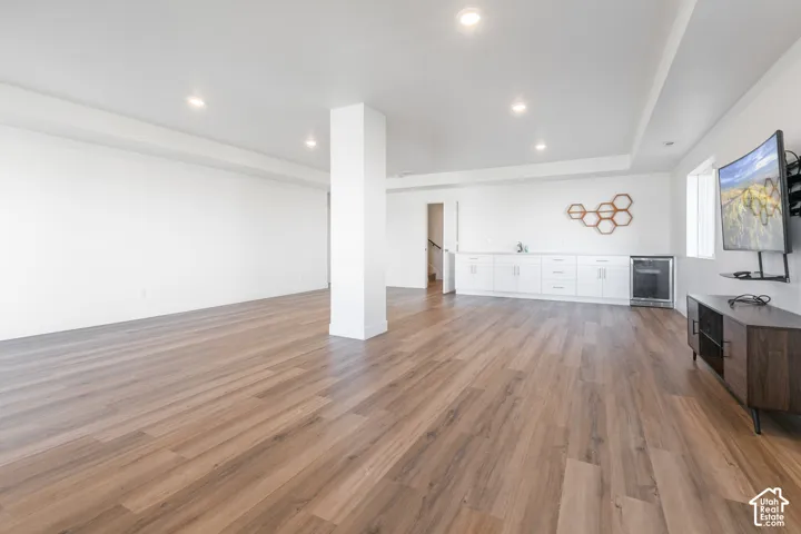 Expansive open-concept room featuring wood-finish flooring, recessed lighting, and a built-in wet bar with white cabinetry and an under-counter beverage refrigerator