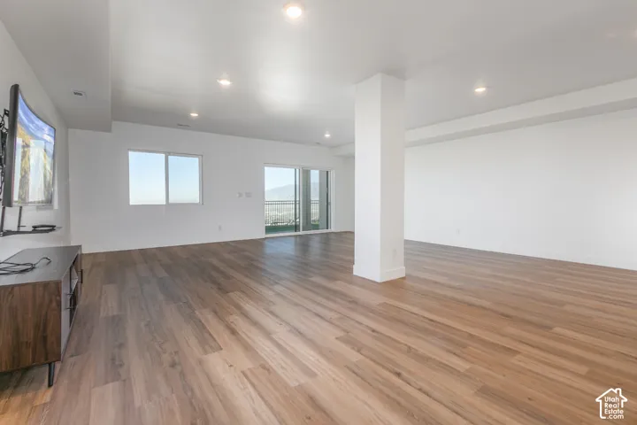 Expansive open-concept room featuring wood-finish flooring, high ceilings, recessed lighting, and a large sliding glass door