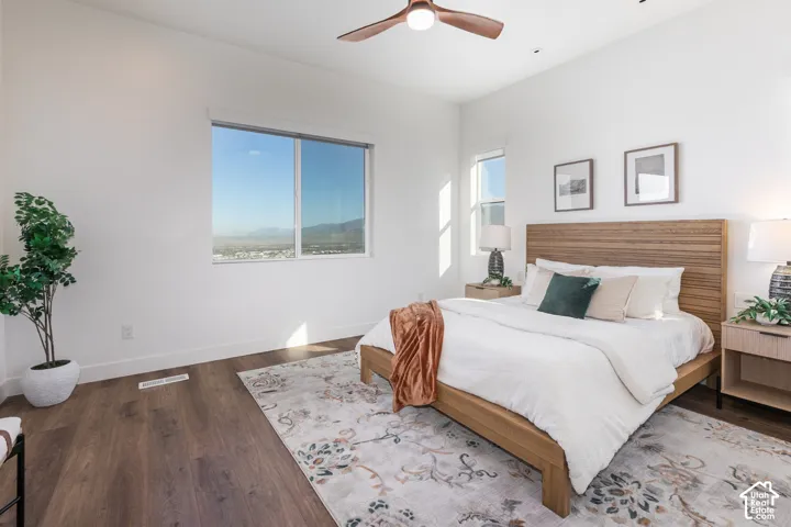 Spacious primary bedroom with wood-finish flooring, a wood-frame bed with upholstered headboard, and expansive windows offering natural light and panoramic vistas