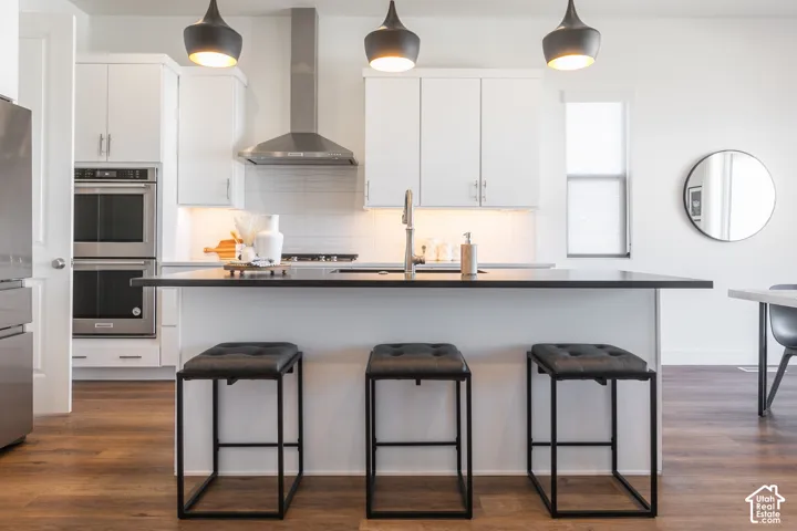 Modern kitchen featuring white cabinetry, stainless steel appliances, a center island with countertop seating, wood-finish flooring, and pendant lighting