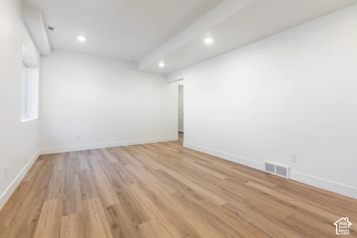Bright, open room with pristine white walls, recessed ceiling lighting, and beautiful wood-finish flooring throughout