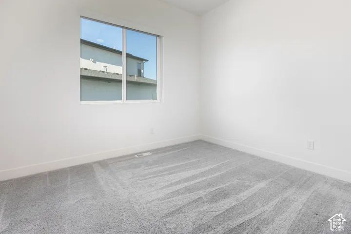Bright corner bedroom featuring expansive windows with natural light, neutral wall finishes, and plush carpeting with linear pattern detailing