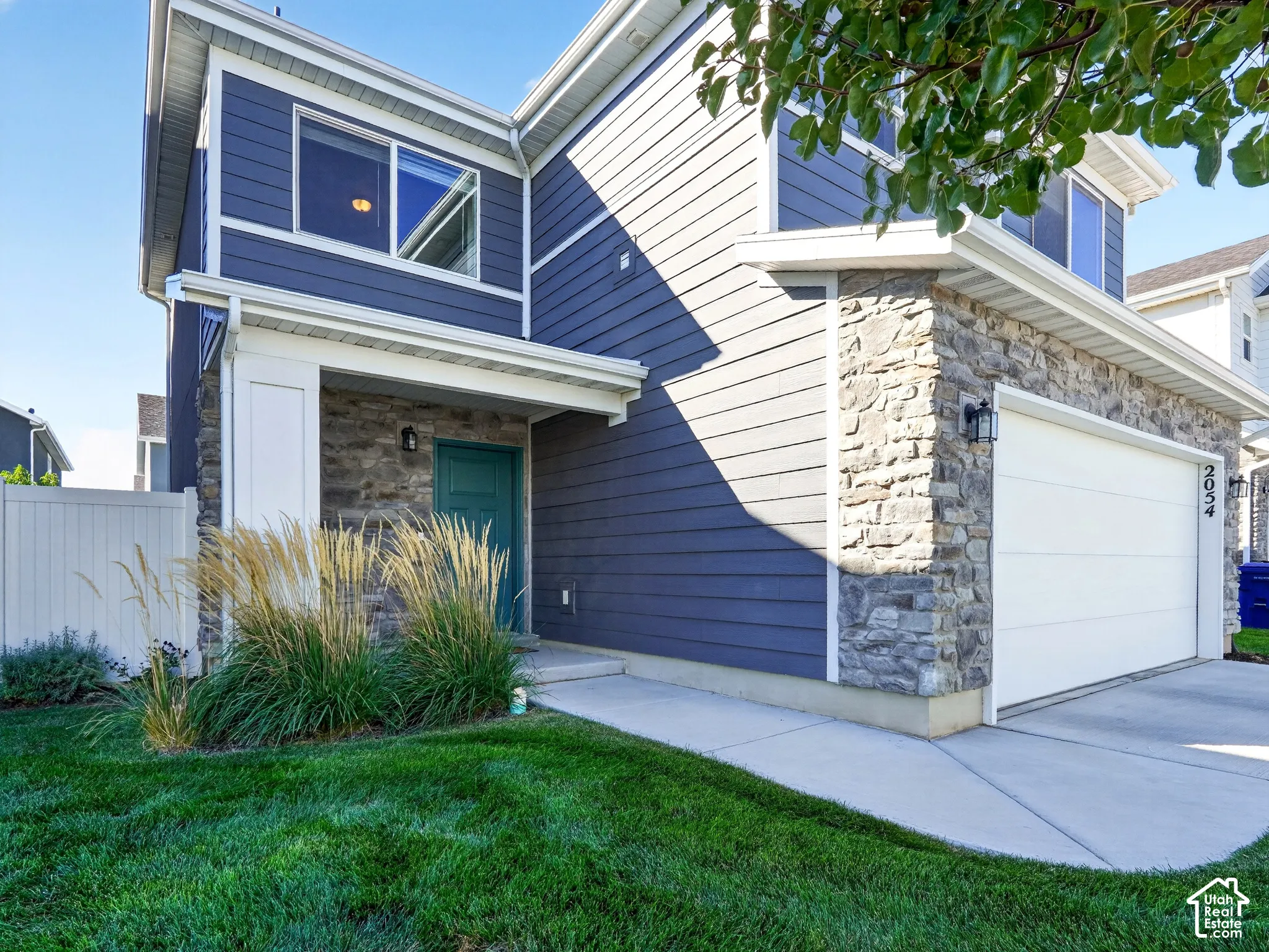 Exterior featuring blue siding, stone facade accents, a teal entry door, white garage door, and concrete driveway
