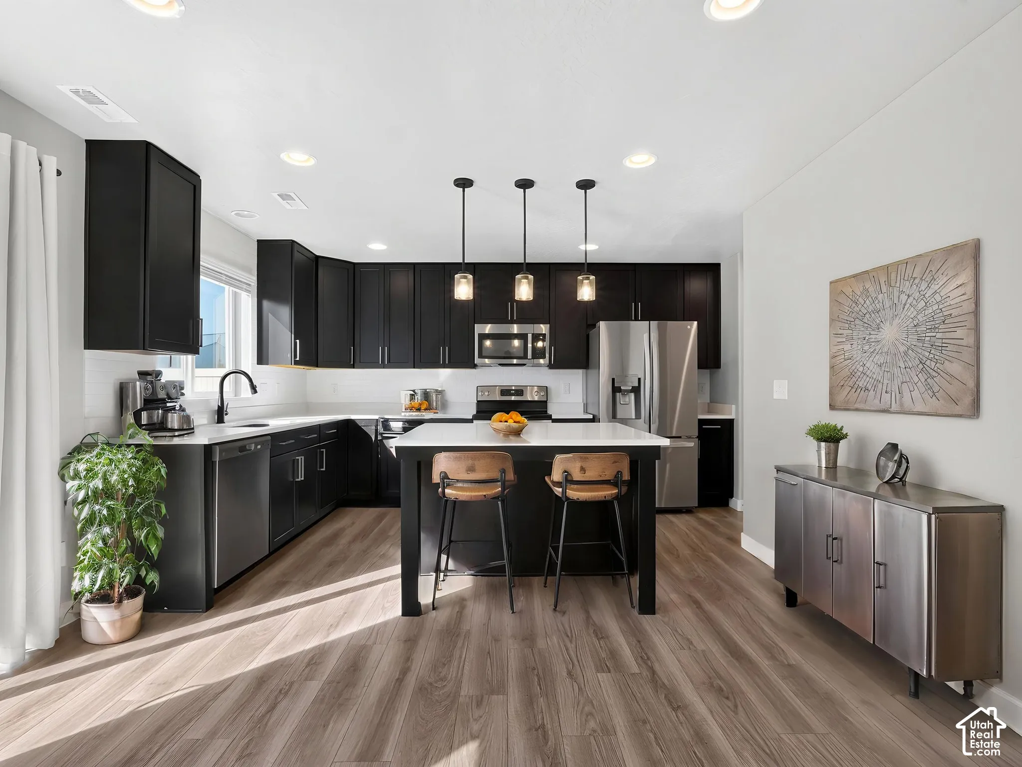 Kitchen featuring dark cabinetry, white countertops, stainless steel appliances, a center island with pendant lighting, and wood-finish flooring