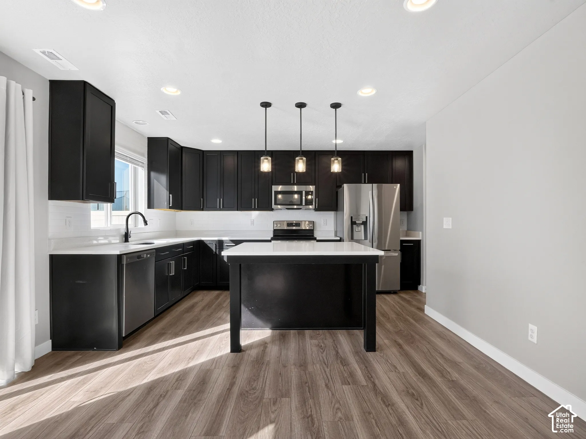 Kitchen featuring dark cabinetry, white countertops, a central island with pendant lighting, stainless steel appliances, and wood-finish flooring