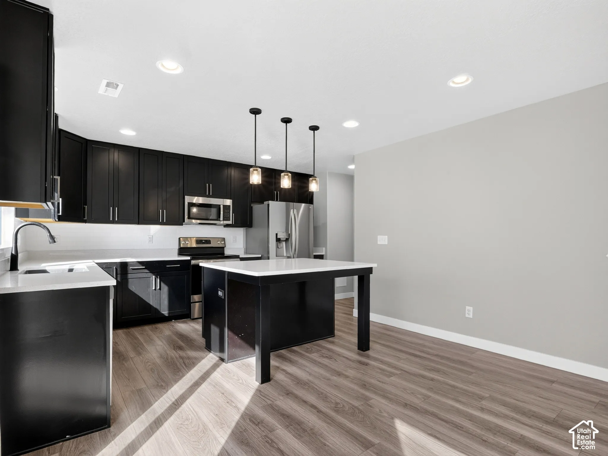 Kitchen featuring dark cabinetry, light countertops, wood-finish flooring, stainless steel appliances, and an island with pendant lighting
