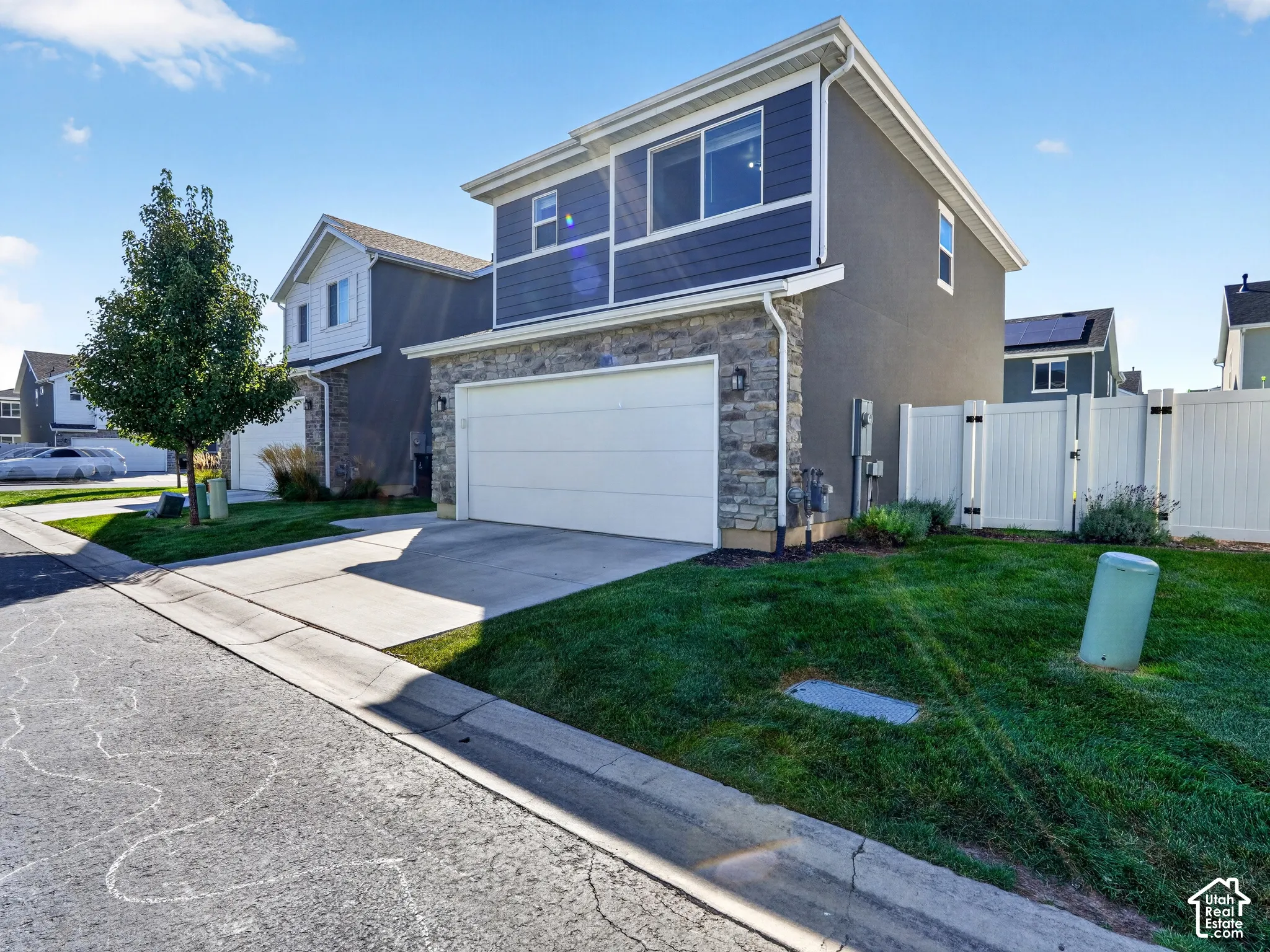Contemporary exterior featuring a stone and siding facade, attached two-car garage, concrete driveway, and a white privacy fence