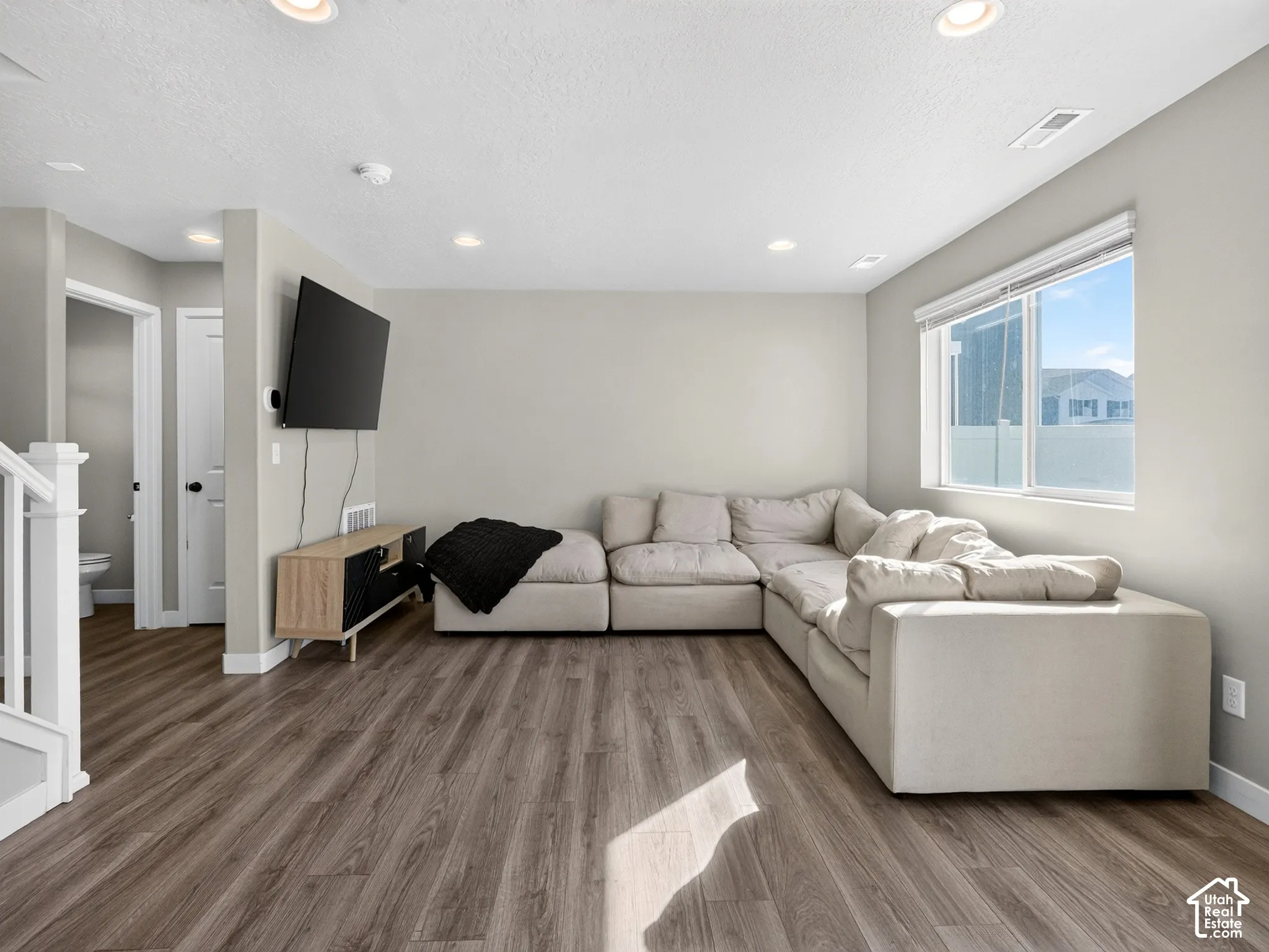 Wood-finish flooring throughout, recessed ceiling lighting, a white painted staircase, and a window with roller blinds