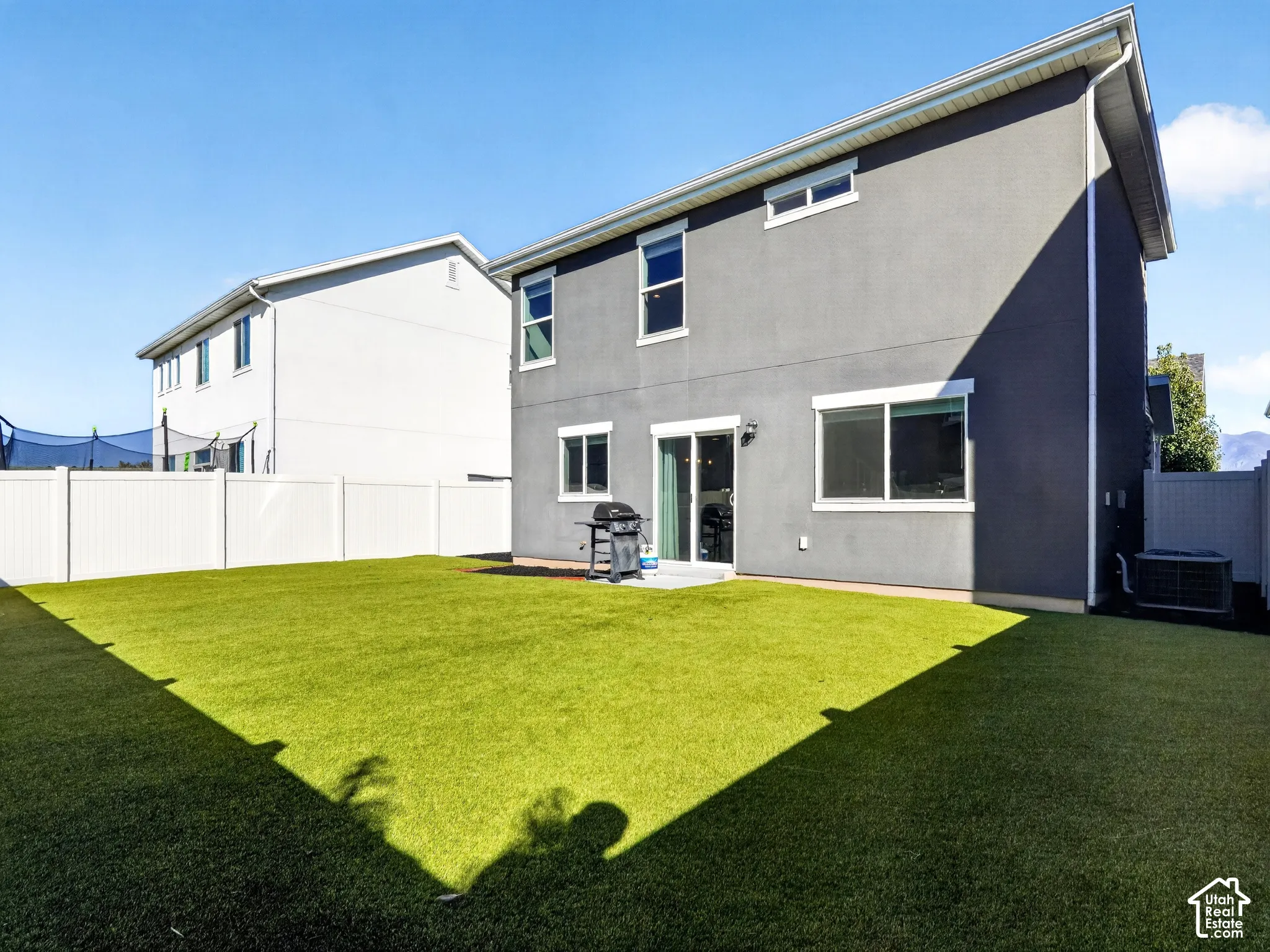 Expansive artificial turf backyard with privacy fencing, a ground-level patio, and a sliding glass door entry