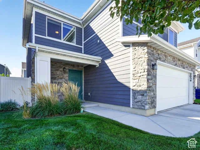 Exterior featuring blue siding, stone facade accents, a teal entry door, white garage door, and concrete driveway