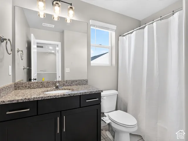 Bathroom featuring a vanity with a granite-style countertop, a rectangular undermount sink, dark wood-finish cabinetry with silver-tone hardware, and a window with blinds