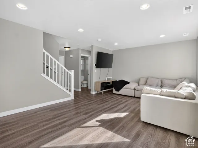 Wood-finish flooring, recessed ceiling lighting, light gray wall finishes, white stair railing, and a white toilet