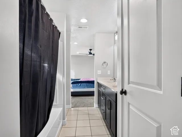 Bathroom featuring a shower-tub combination, single vanity with dual sinks, dark wood-finish cabinetry, and tile flooring