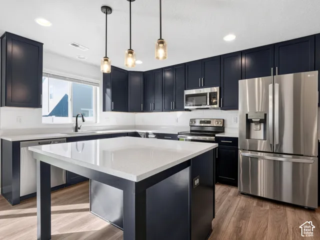 Kitchen featuring dark cabinetry, stainless steel appliances, a center island with a light-toned countertop, a subway tile backsplash, and wood-finish flooring