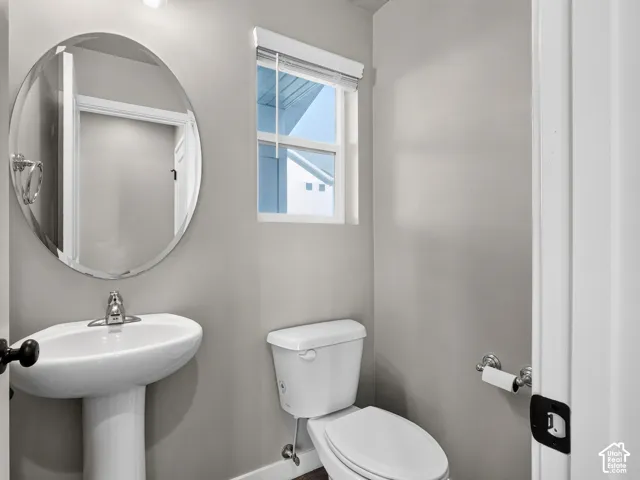 Pedestal sink with chrome faucet, oval wall mirror, and toilet