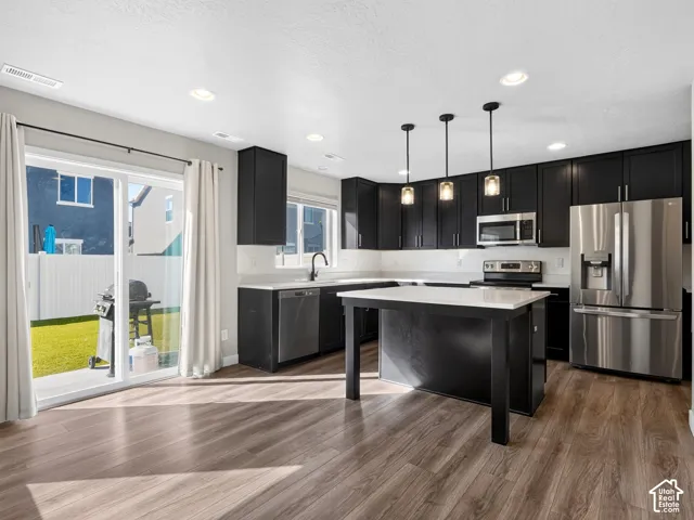 Modern kitchen featuring dark cabinetry, stainless steel appliances, a center island with a light-toned countertop, and wood-finish flooring