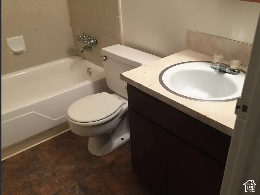 Bathroom featuring a white bathtub, ceramic tile surround, toilet, vanity with integrated sink, and tile flooring