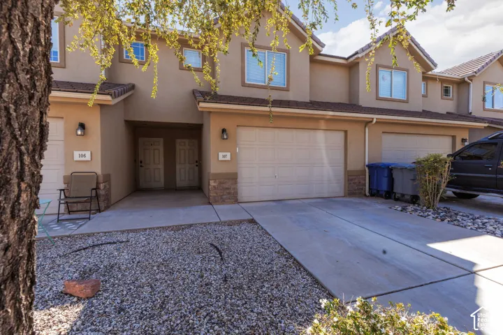 Stucco exterior with stone accents, two-car garage, concrete driveway, and natural rock landscaping