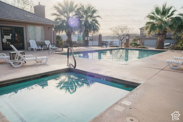 Swimming pool and spa with surrounding concrete decking, complemented by mature palm trees and adjacent building with a tile roof