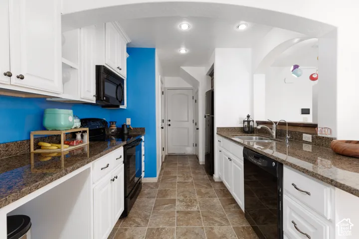 Kitchen featuring white cabinetry, dark stone-finish countertops, black appliances, and neutral-toned floor tiling