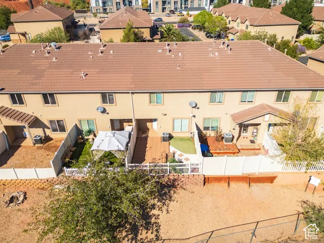 Rear elevation with multiple windows, private fenced patios, and a mix of hardscaping and artificial turf