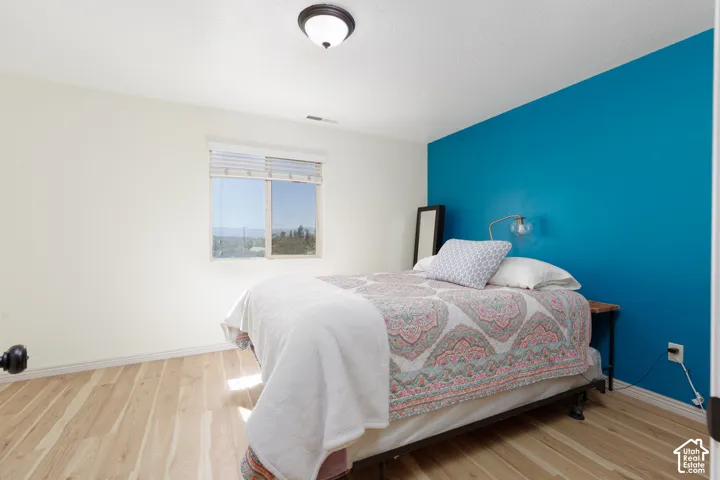 Wood-finish flooring, accent wall, window with blinds, ceiling-mounted light fixture, and white wall finishes