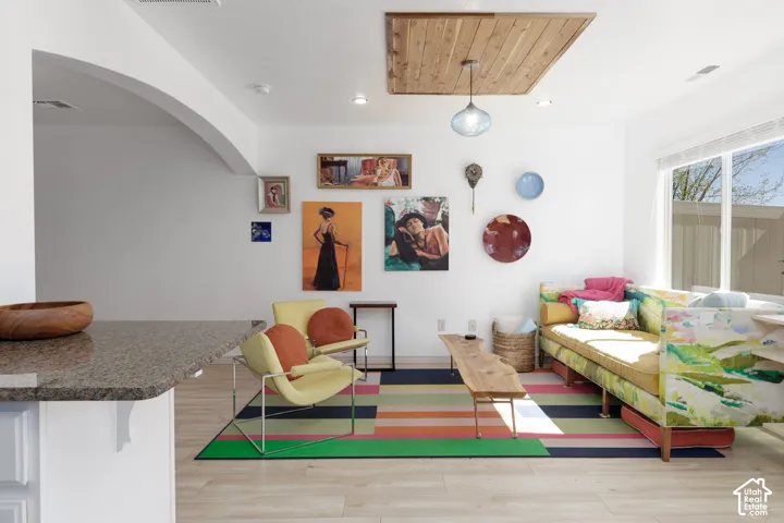 Light wood-finish flooring, white walls, arched doorway, recessed lighting, and a suspended light fixture with a wood ceiling accent