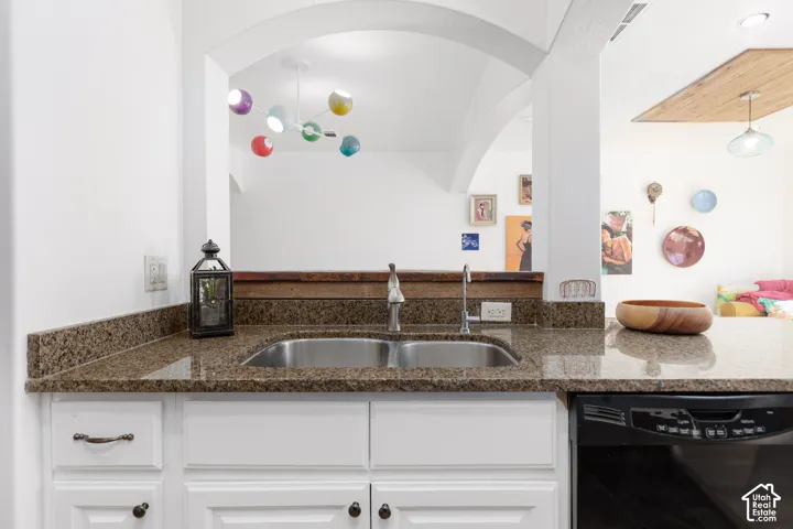 Granite countertops, stainless steel dual basin sink, white cabinetry, integrated dishwasher, and a colorful suspended light fixture