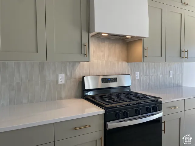 *COMPARABLE HOME, EXAMPLE OF LISTING AFTER COMPLETION. Stainless steel gas range, light gray shaker-style cabinetry, white countertops, tile backsplash, and a built-in range hood
