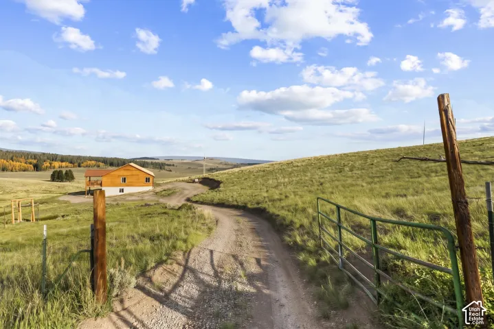 Exterior: A gated entrance and gravel drive lead to the cabin across the open meadow.