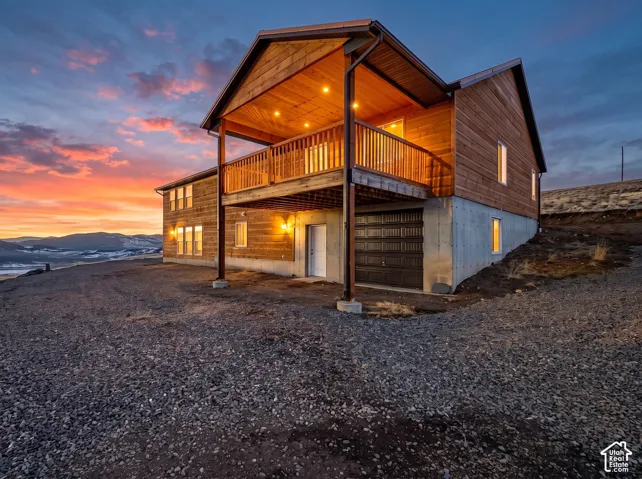 Exterior: The large covered deck off the primary bedroom sits above the snowmobile/storage garage, lit for a mountain sunset.