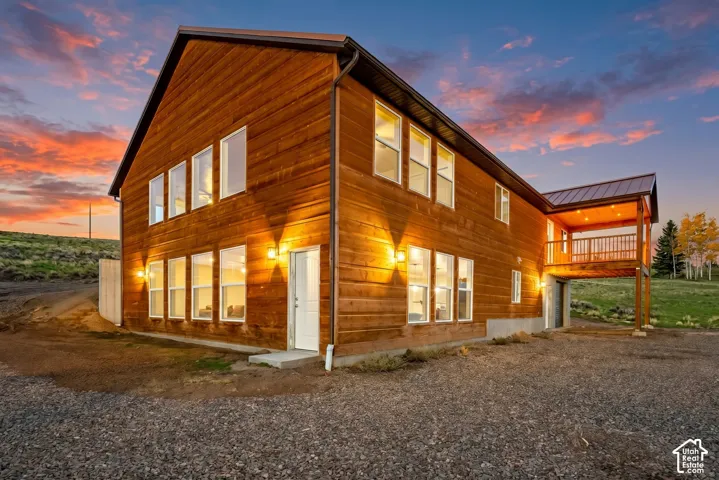 Exterior: Wood lap siding, a metal roof, and walls of windows glow at dusk on this two-level cabin set into the hillside.