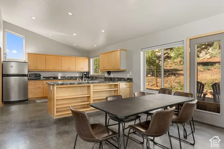 Vaulted ceiling, recessed lighting, wood-finish cabinetry, stainless steel refrigerator, and ample natural light