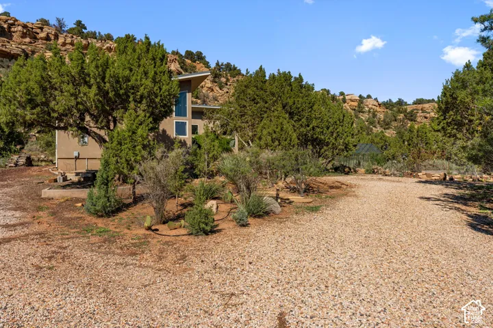Stucco exterior with a metal roof and prominent vertical windows, surrounded by mature trees and natural landscaping