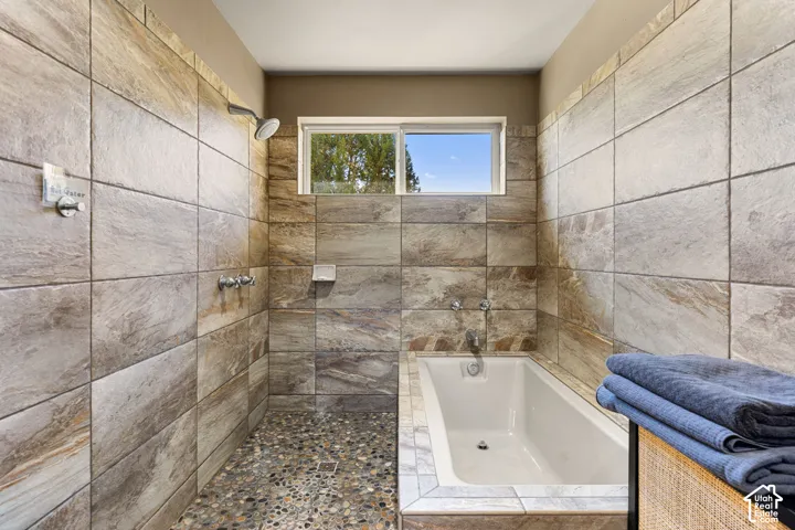 Tiled shower enclosure with a pebble floor, integrated bathtub, and a window