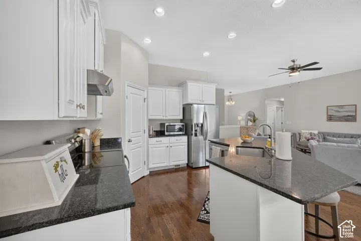 White cabinetry, dark stone countertops, stainless steel appliances, wood-finish flooring, and recessed lighting