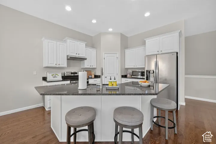Kitchen featuring white cabinetry, dark stone countertops, stainless steel appliances, recessed lighting, and wood-finish flooring