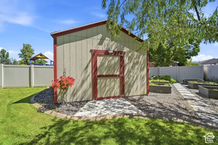 Detached storage shed with board and batten siding, fully fenced yard, raised garden beds, gravel hardscaping, and a concrete path
