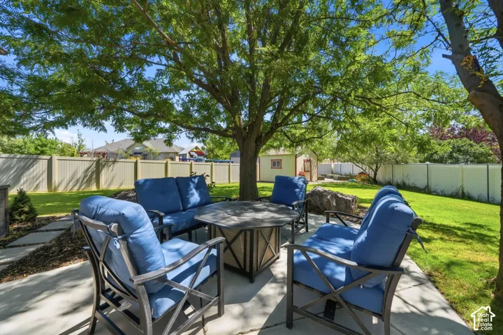 Expansive patio area with concrete surfacing, shaded by mature trees, featuring a privacy fence, and a distant storage shed